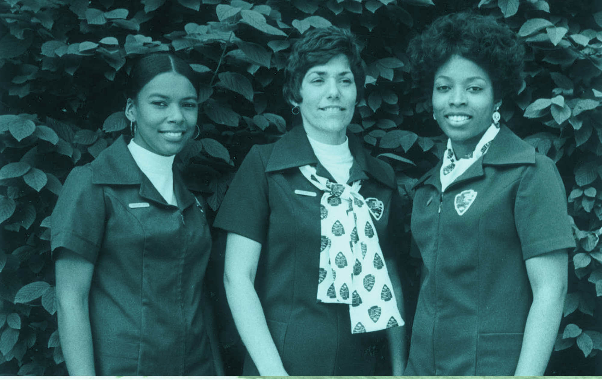 Three women pose in NPS uniforms. Two wear pantsuits and one a dress. The uniforms have arrowhead patches instead of ranger badges.