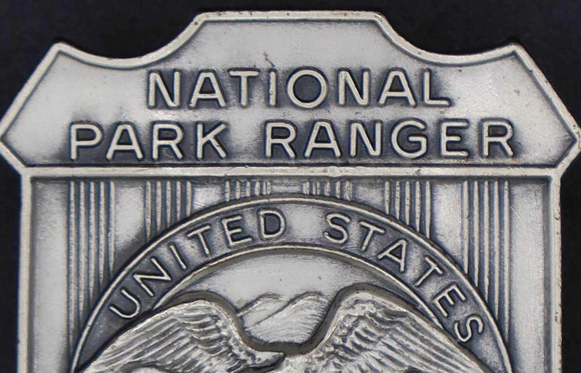 Silver shield-shaped badge marked National Park Ranger. The round seal in the middle has an eagle looking to its right.