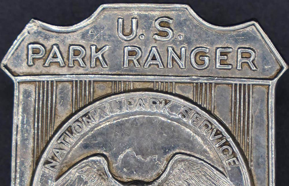 Silver shield-shaped badge marked U.S. Park Ranger. The raised round seal in the middle has an eagle looking to its left.