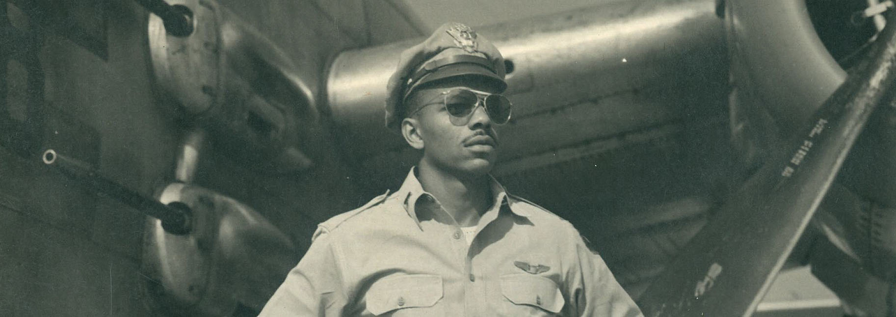 Photograph of Col. Mulzac in uniform shaking a gentleman's hand in front of an exhibit panel created in his honor at the John F. Kennedy International Airport in New York City. >
			<div class=