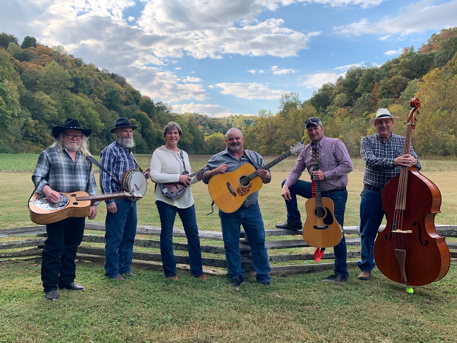 Six musicians with instruments standing in front of a split rail fence