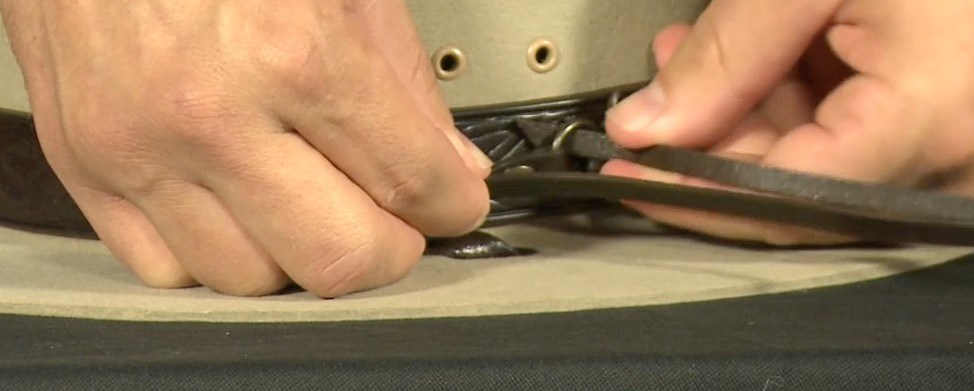 Tying the Hatband Step 2 A close-up of hands feeding a cord through the rings of a hatband on a ranger hat