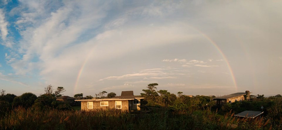 Rainbow at Fire Island National Seashore A rainbow is visible across a partially hazy and partially clear sky above houses glistening in the morning sunlight