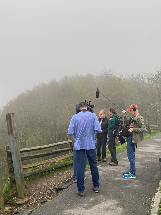Crew with filming and sound recording equipment on a foggy overlook