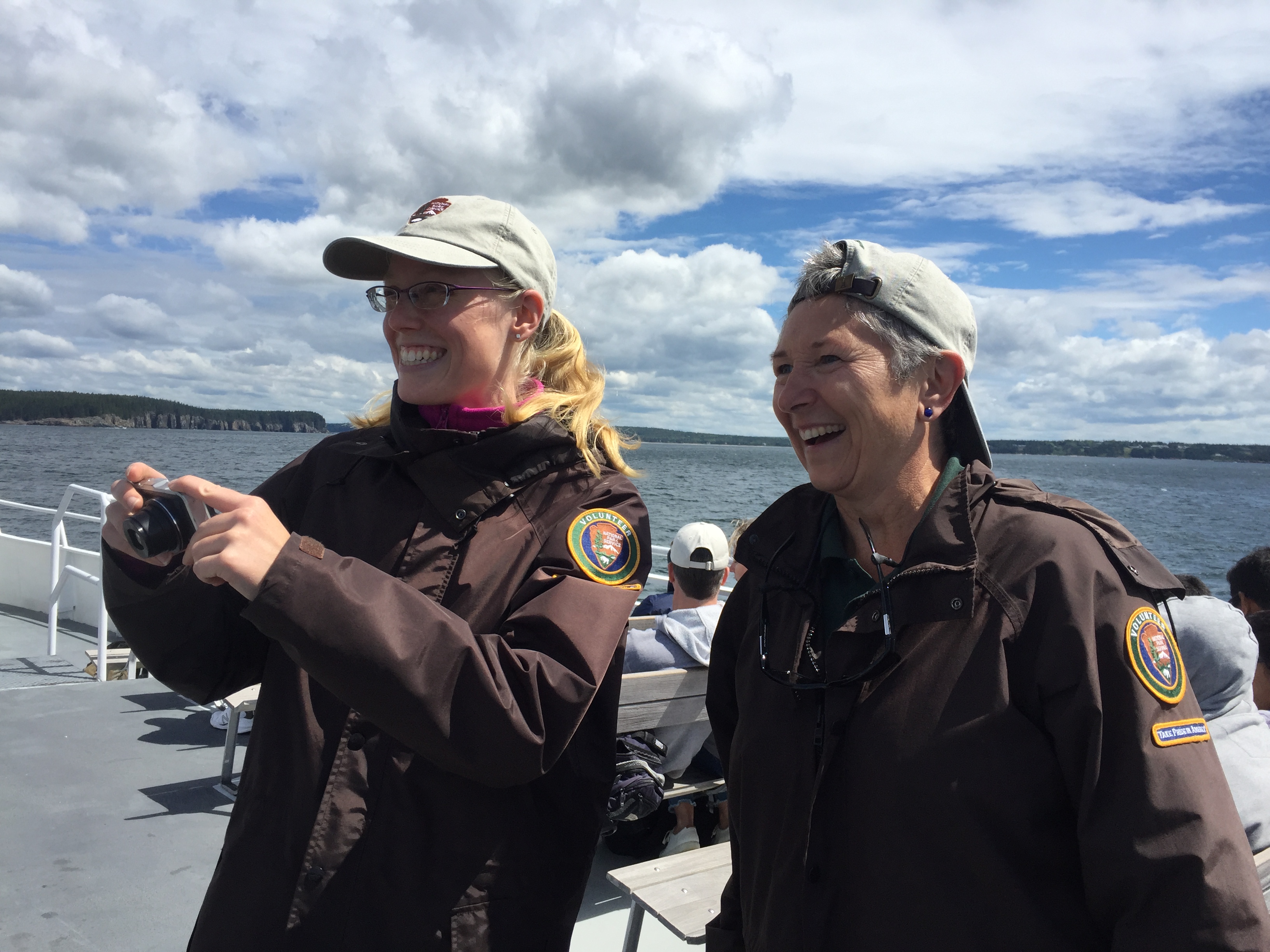 Two women in park volunteer jackets stand on the deck of a large boat