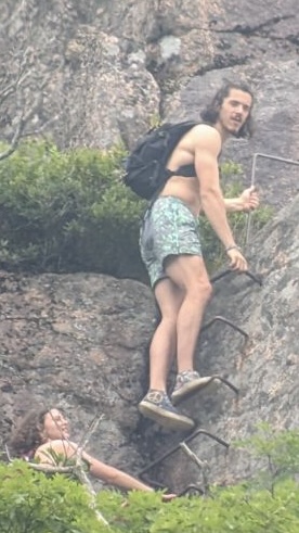 Suspects appear to scale iron rungs on the east face of Champlain Mountain. First suspect presents as male has shoulder length dark wavy hair and facial hair. A woman with dark curly hair follows behind.