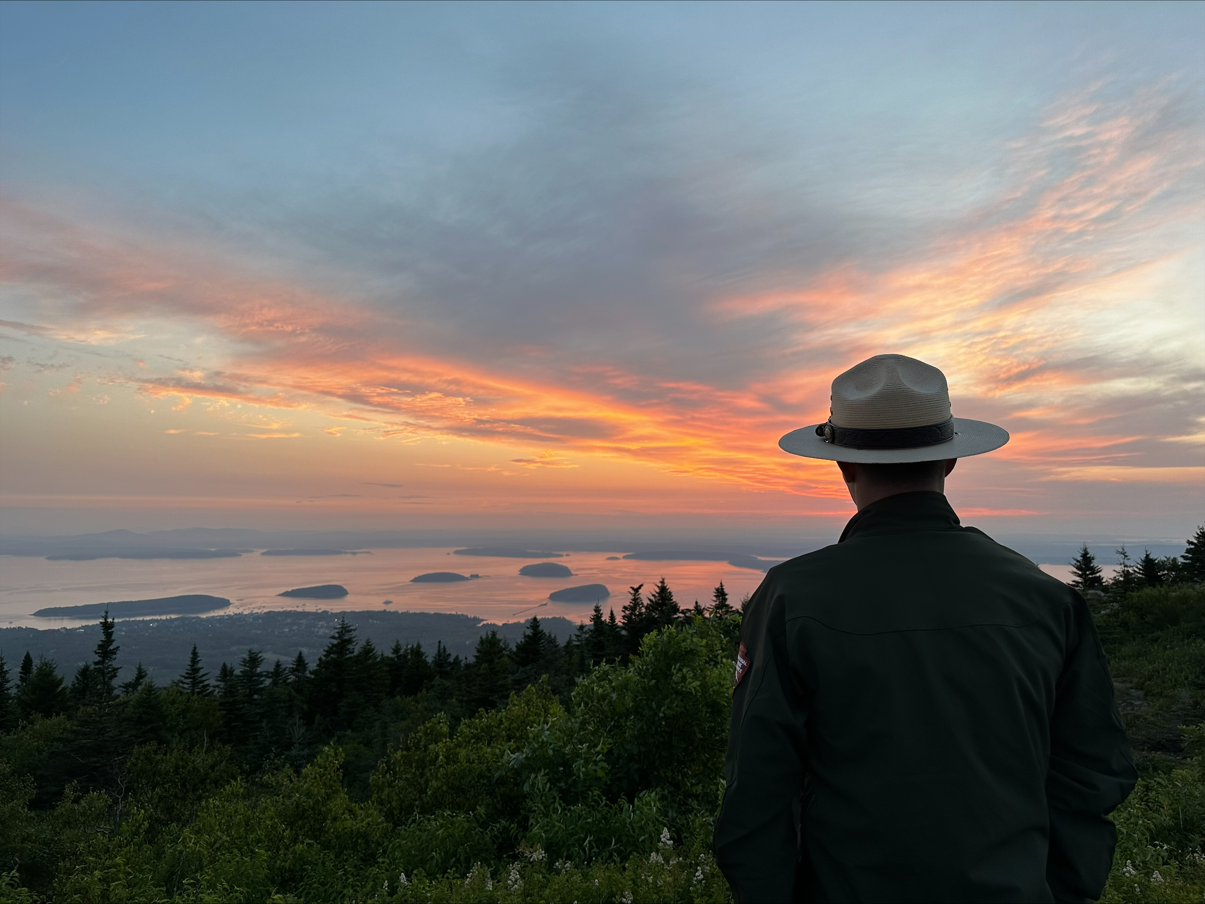 Park ranger at the top of Cadillac Mountain watches sunrise over Frenchman Bay