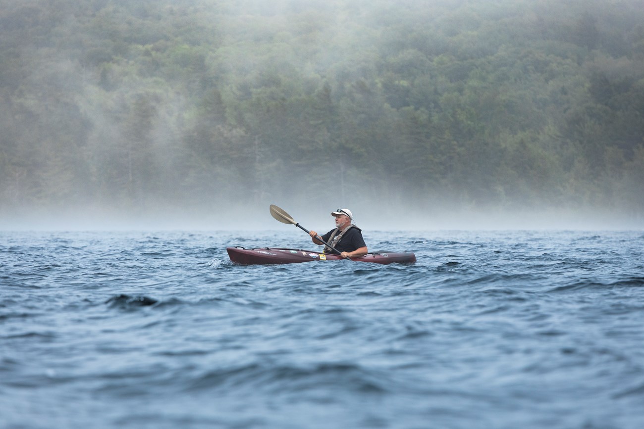 Kayaker paddling on a foggy Eagle Lake with a misty forest.