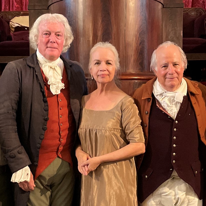 Two men and one woman wearing clothing in the style of the late 1700s and early 1800s