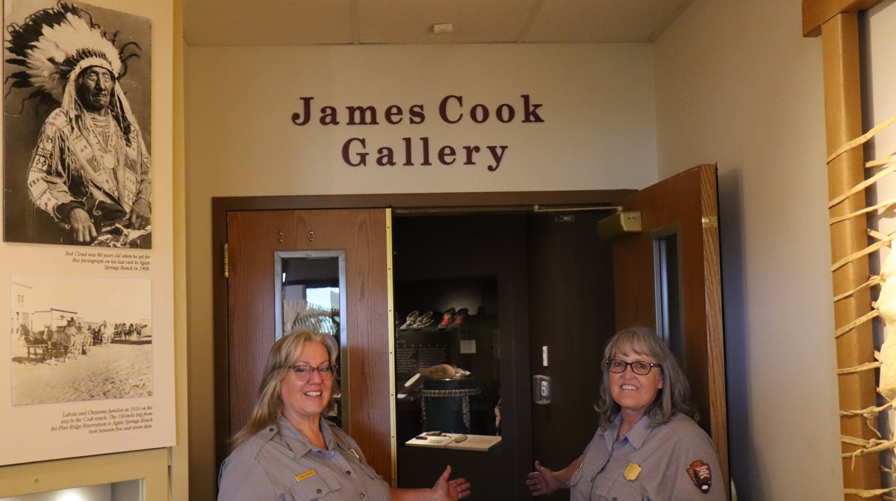 Two smiling female rangers stand by the open door to the Cook Exhibit.