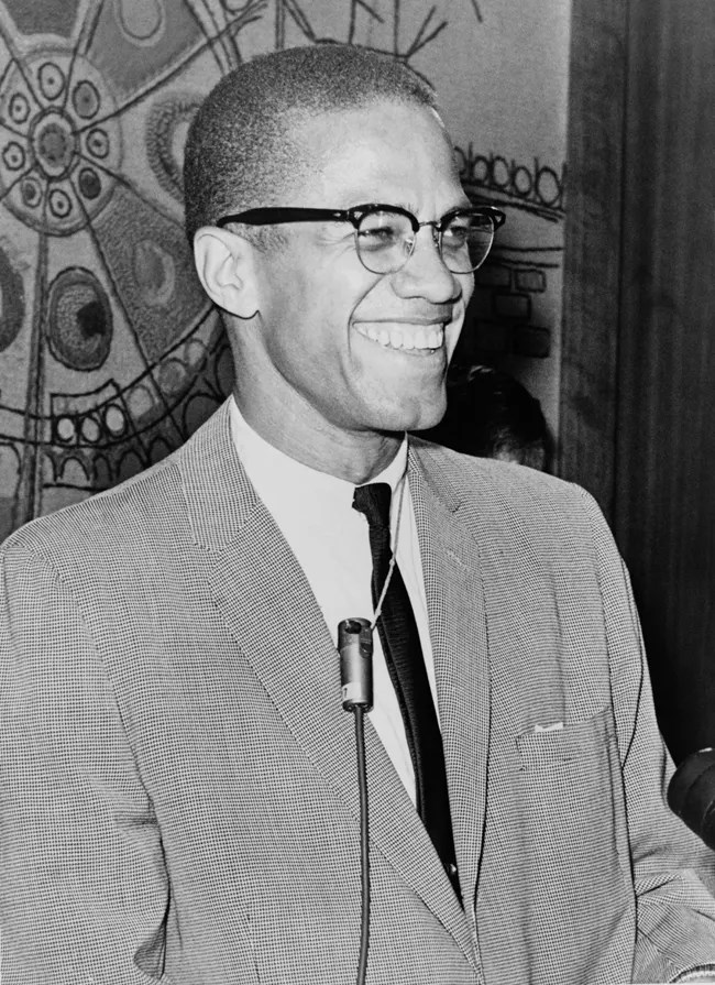 A man in a coat and tie stands at a podium. He is smiling.