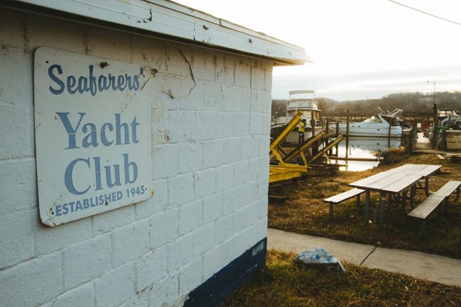 A white sign with blue letters "Seafarers Yacht Club" "Established 1945"