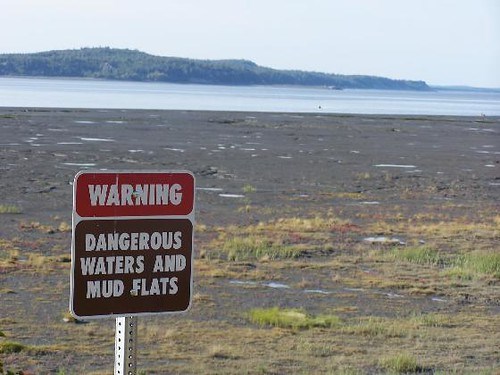 Warning signage for Dangerous Waters and Mud Flats, with mudflat of Cook Inlet in background.