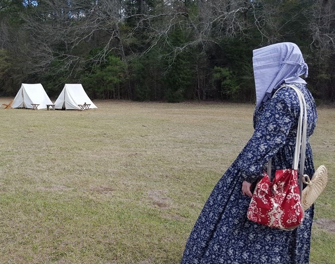 Woman in period dress looking at white tents and camp chairs