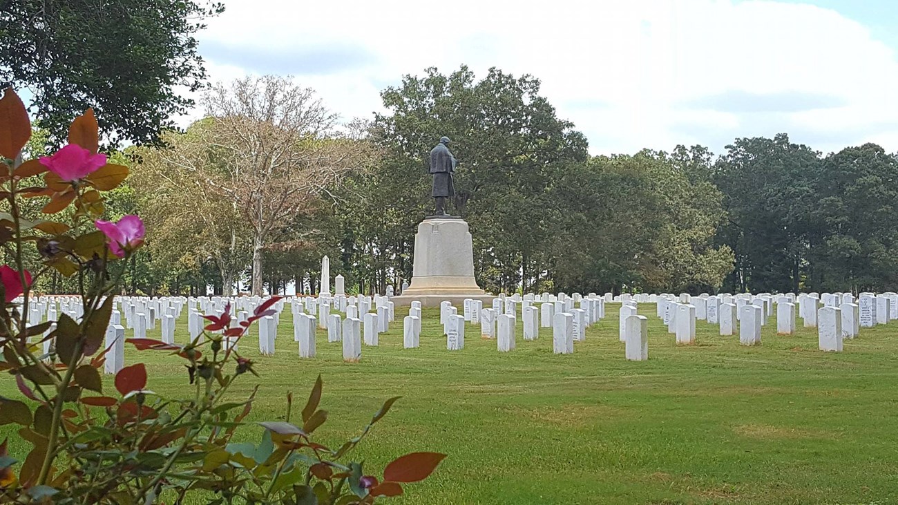 Cemetery with headstones, statue of a soldier, trees, and a rosebush