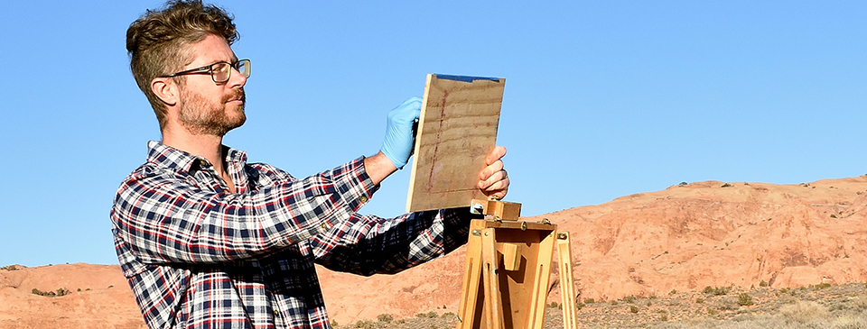 a man holds up a board next to an easel