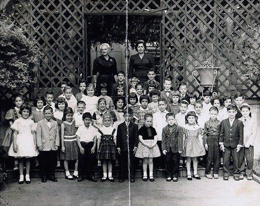Rows of children standing on steps in front of a Sukkah. Two women stand behind the children.