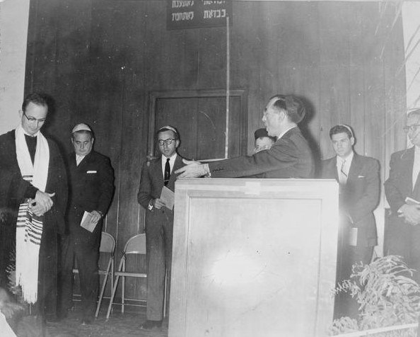 Rabbi Sanders Tofield speaking to six men surrounding him and listening.