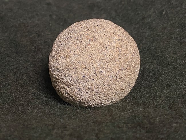 A nearly round sandstone concretion, about the size of a golf ball, is sitting on a piece of green fabric.