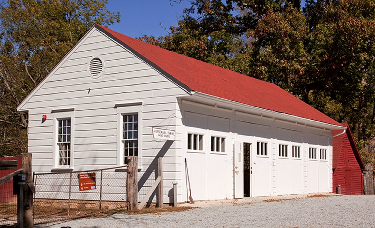 A white garage  with a red roof and several doors holds a few vehicles and farm equipment
