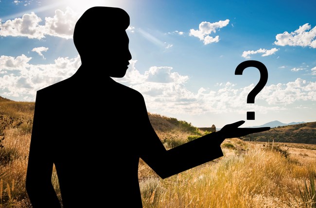 A silhouette of a man appearing to hold up a large question mark, superimposed over the top of a color photo of the golden grasslands around Great Falls, Montana.  The sky has sunshine with cumulous clouds and a small mountain peak can be seen in the far