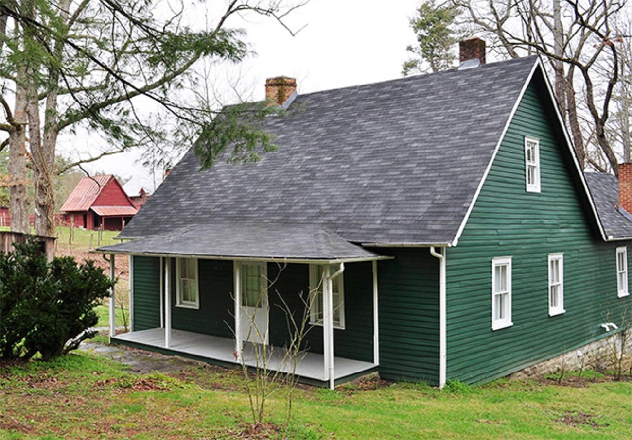 Green farm house with front porch and outbuildings