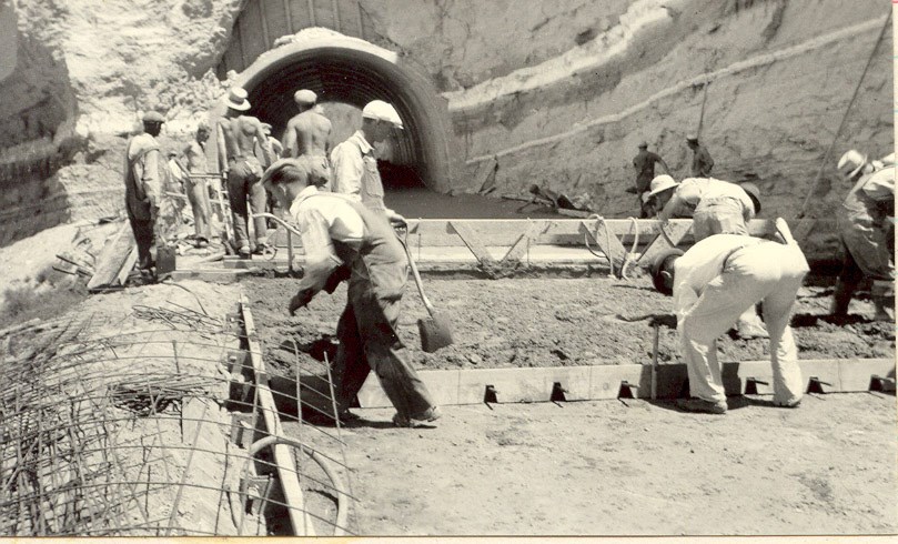 A large group of men work with newly poured wet concrete.