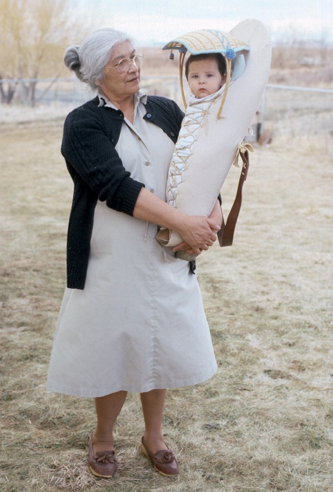 Shoshone elder Martha Dick pictured here with her grandson, Bodagwitche, in Owyhee, Nevada in 1986. Martha Dick faces the camera; her grandson is in a cradleboard in her arms.