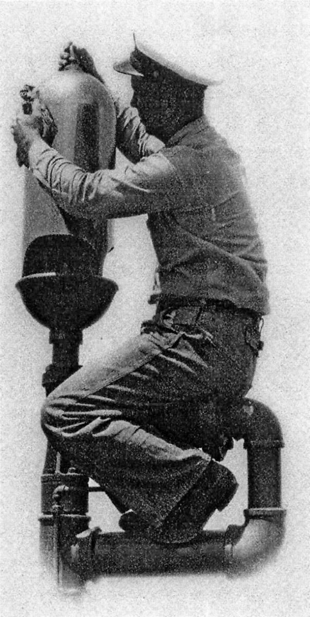 A black and white photo of a man bent over fixing an air whistle dog signal device.