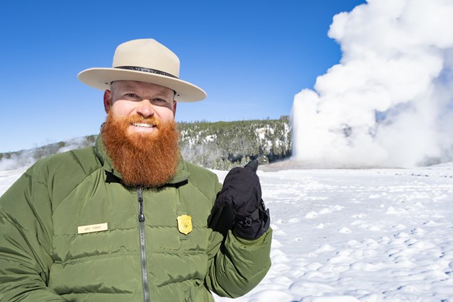 A park ranger motions to Old Faithful Geyser erupting in the background.