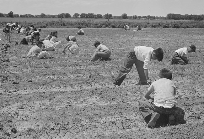 Children kneel in a dirt field.