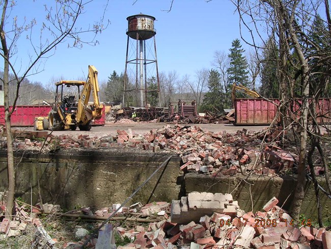 Jaite Mill demolition Below a rusting water tower, backhoes move stacks of bricks into red dumpsters.