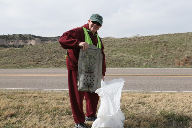 A man wearing a high-visibility vest, clean up litter along a road.