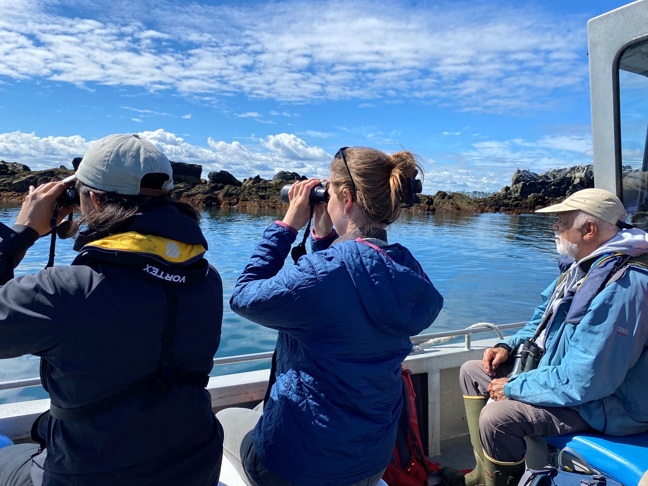 Three people on a landing craft searching for birds on a nearby island.