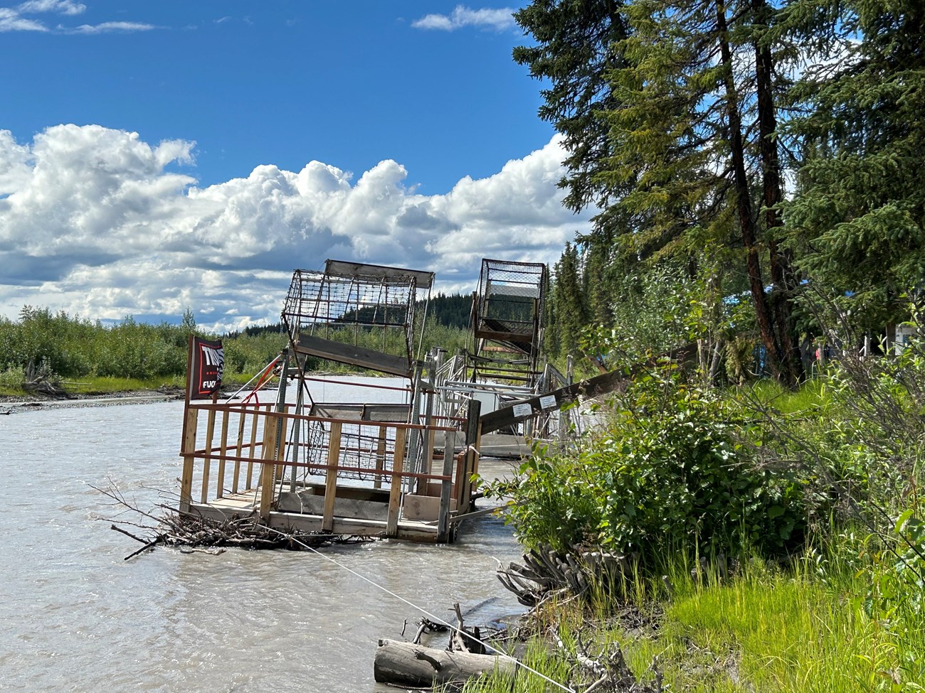 Fish Wheel Two structures, with large, metal baskets are operated in the river, near the bank.