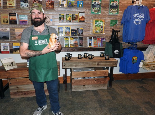 A man wearing a green apron stands in a store holding a stuffed animal.