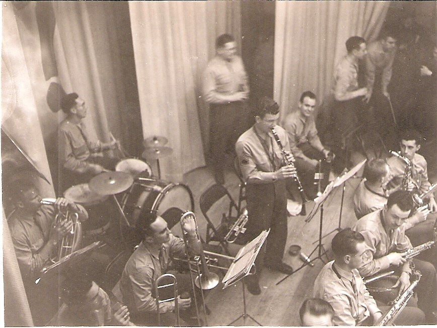 Group of men seated and standing, with brass instruments in a hall.