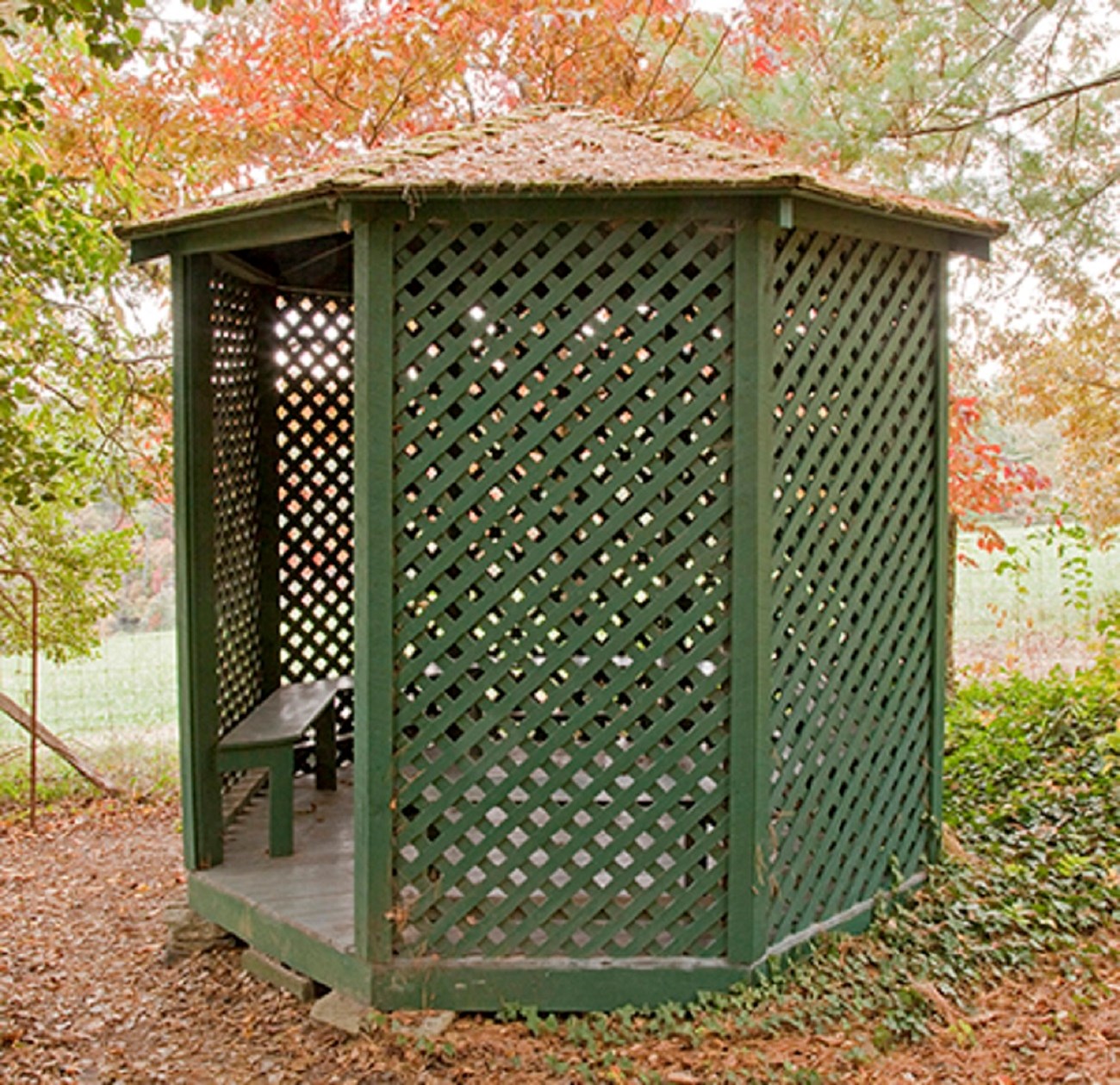 A small octagonal shaped building with green lattice and benches inside