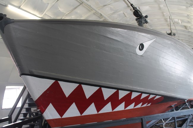Boat with shark mouth, teeth, and eyes painted on it.