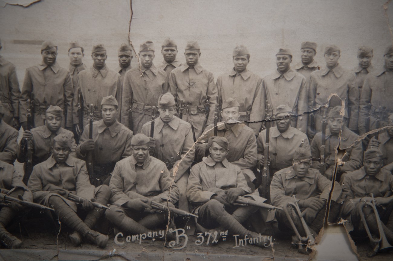 24 Black men of Company B, 372 Infantry Regiment, holding rifles, posing for a photo in France, April 1918.