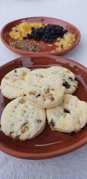 Two plates laid out on white table cloth. One has nicely rounded shortbread cookies. The other one has diced, dried fruit neatly piled on it.