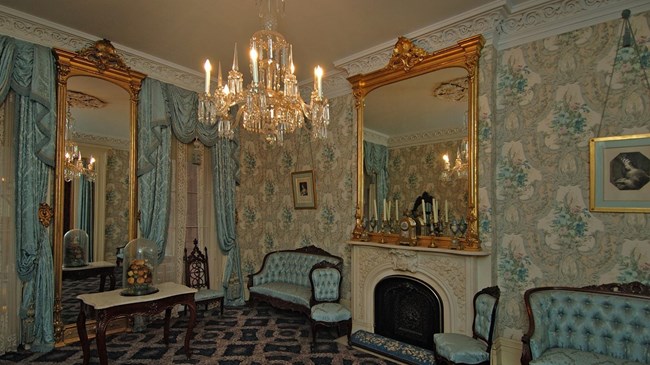 An ornately decorated room with blue wallpaper, a chandelier and upscale old fashioned furniture.