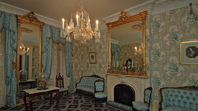 Theodore Roosevelt Birthplace National Historic Site An ornately decorated room with blue wallpaper, a chandelier and upscale old fashioned furniture.