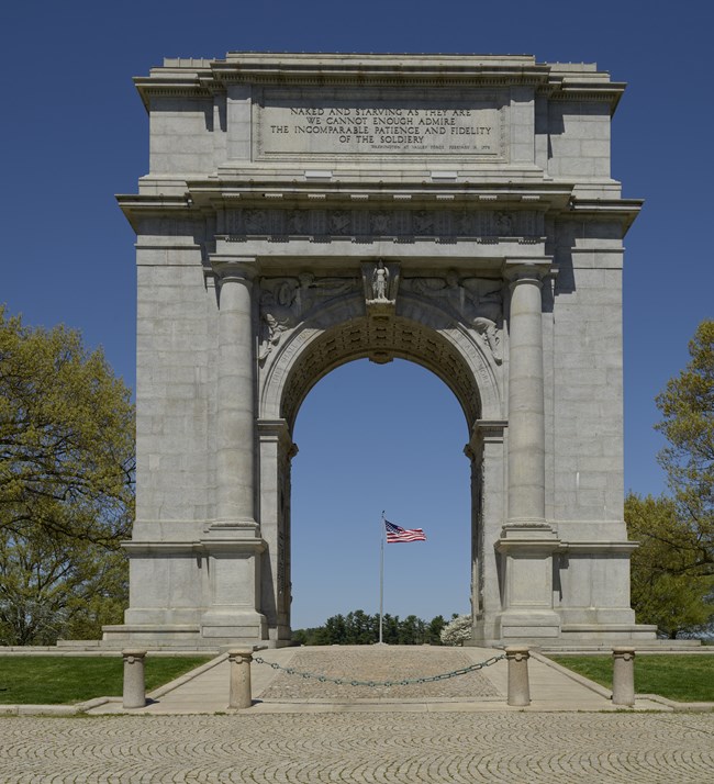 Stone Arch at Valley Forge National Historical Park with American Flag on flagpole visible in distance through the arch