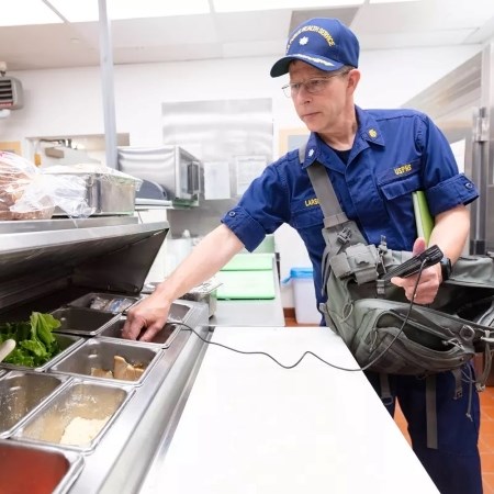 Protecting Public Health a man in uniform testing temperatures of food in an assembly line