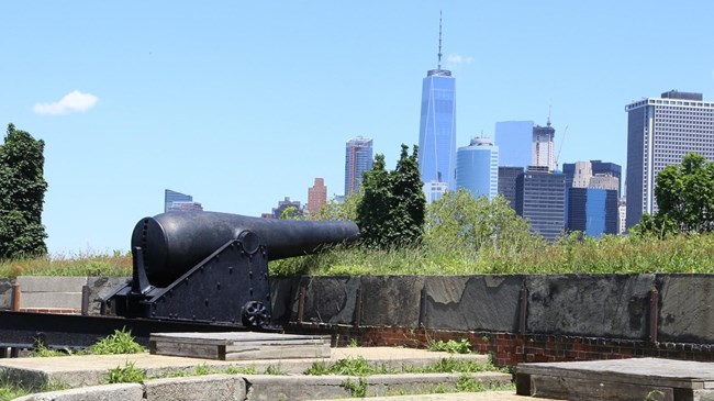 Governors Island National Monument A cannon sits on a wall with a cityscape in the background.