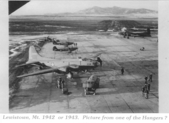 Black and white photo of an airstrip with a propeller plane and mountains in the background