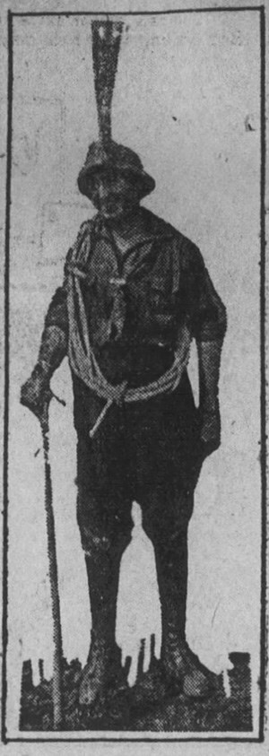 Newspaper photo of Alma Wagen in breeches, shirt, and hat with large plume, holding a walking stick and with a coil of rope around her shoulders.