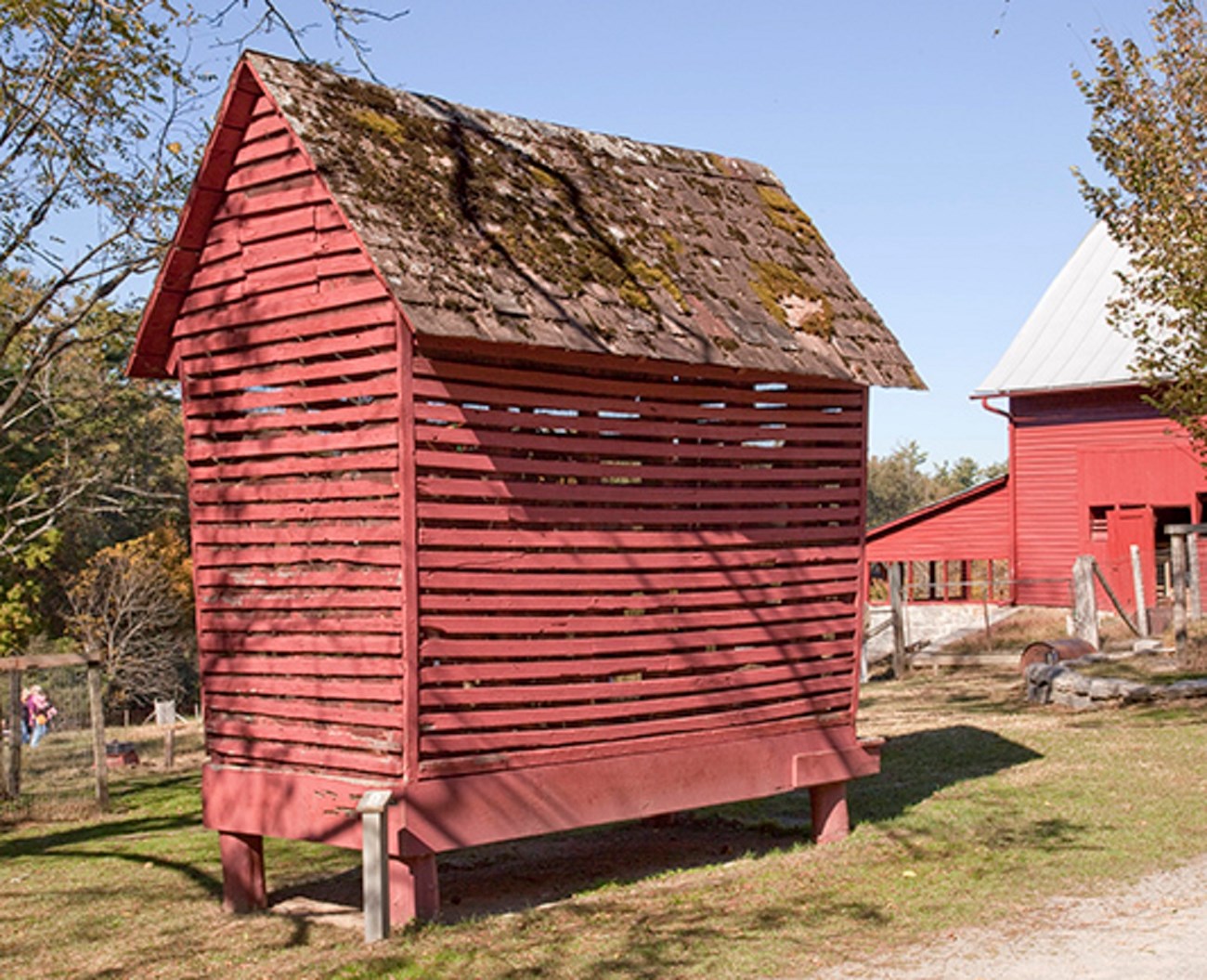 A barn red shed with open wood slats and wire mesh allows air flow.