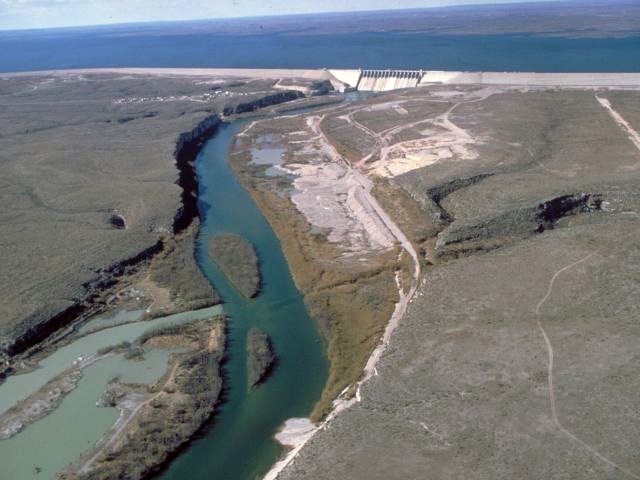 An aerial view of a river meeting a dam and the reservoir beyond it
